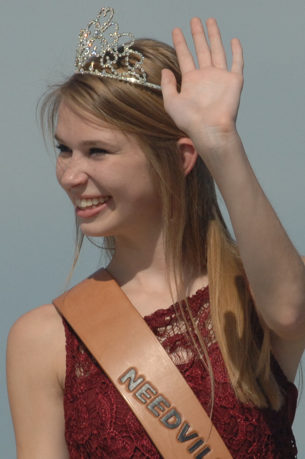 a young lady wearing a crown waves to the crowd