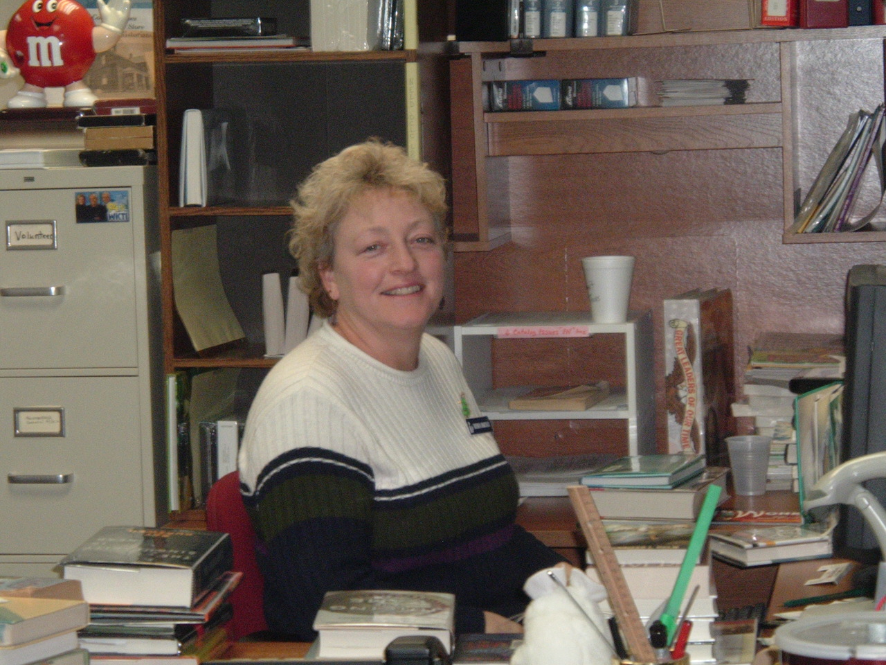 a woman in a sweater smiling and sitting at a desk