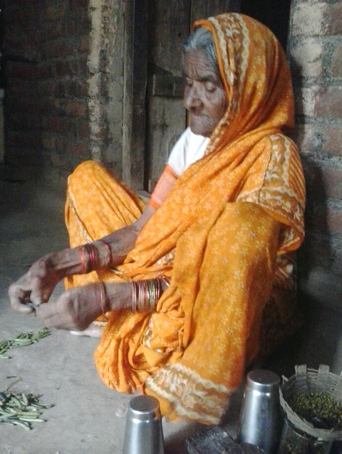 an old woman wearing a yellow sari sitting down on the floor and making soing