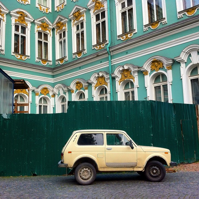 an old yellow pick up truck parked in front of a green building