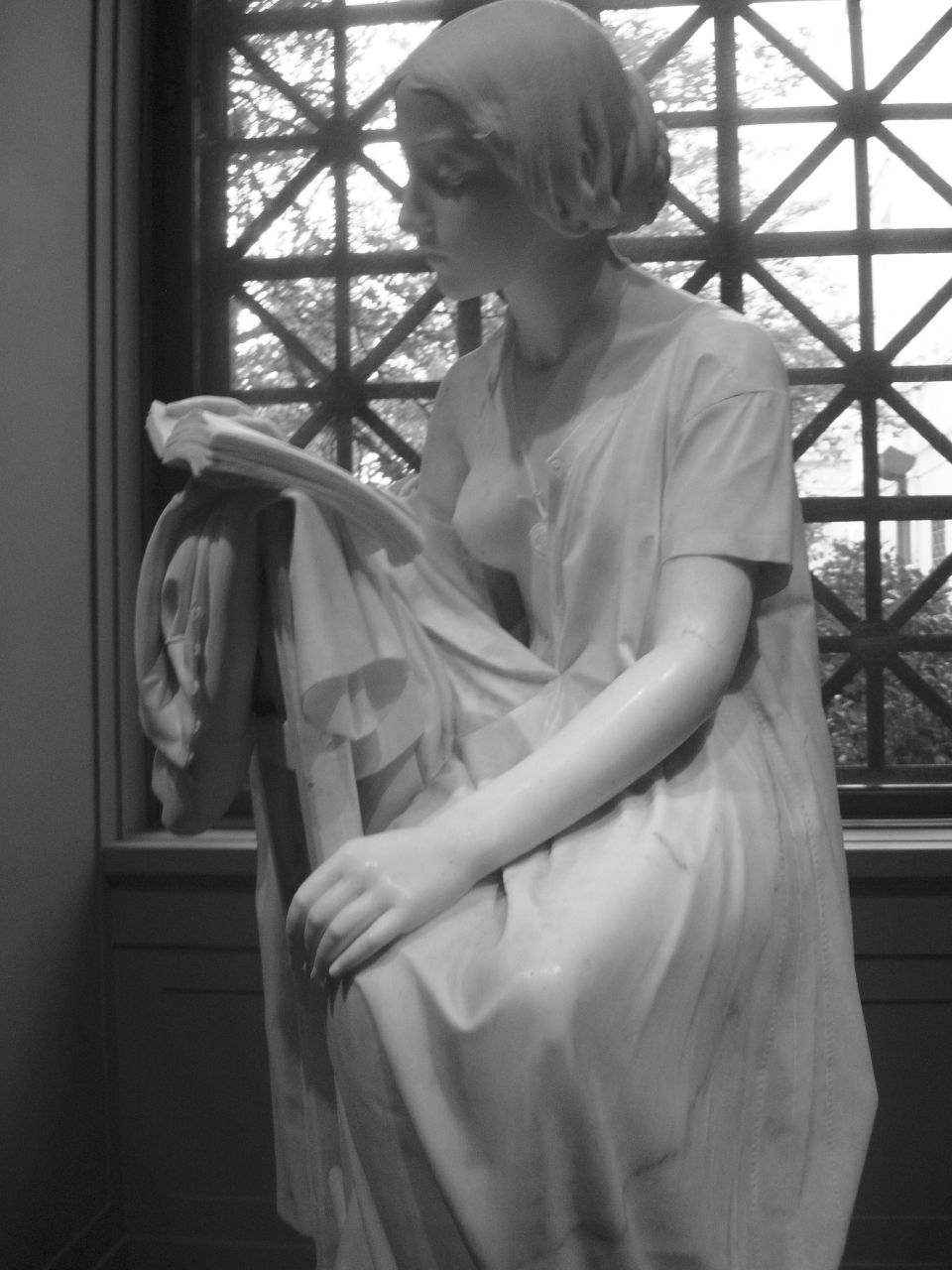 a statue in a white dress is sitting near a window