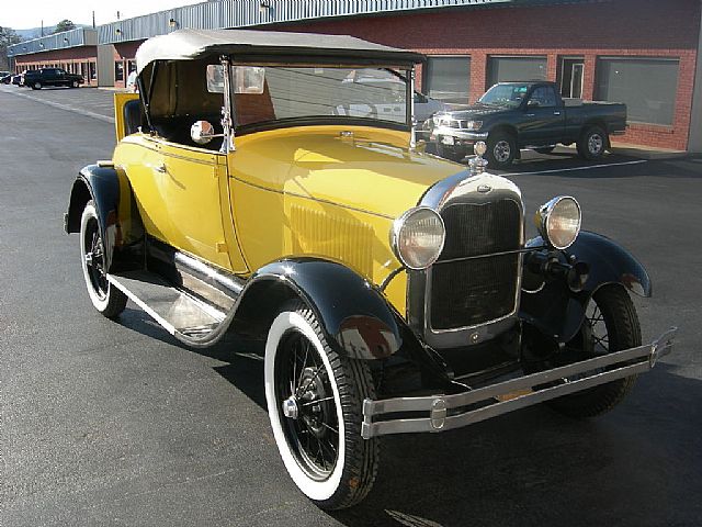 an old yellow and black car sits in a parking lot