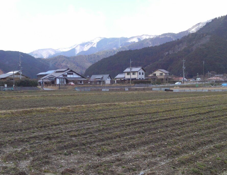 a plowed field next to houses in the mountains