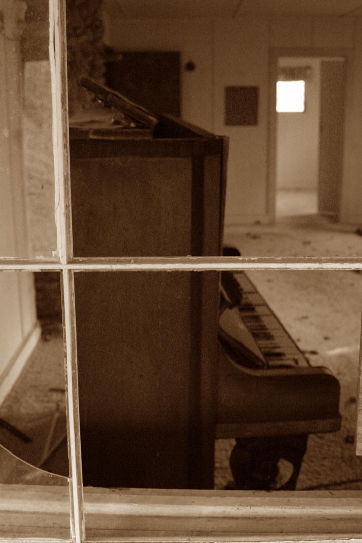 old piano displayed in very dirty room with ed glass panels