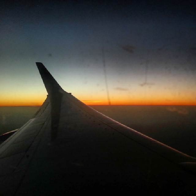 an airplane wing with a dark colored sky and orange sunset