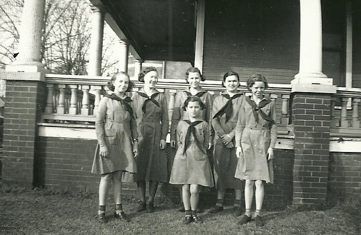 a group of girls dressed in school uniforms posing on the porch