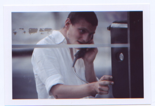 man in white shirt and tie using cellphone while standing by a metal fence