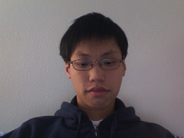 an asian male with glasses posing in front of a wall