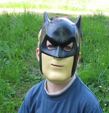 a boy dressed up in a batman mask on the grass