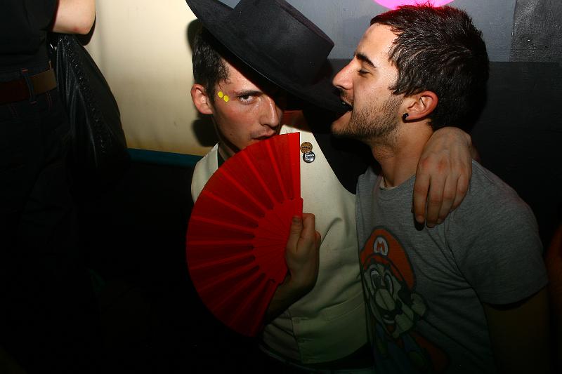 one guy kissing the other while holding a red fan