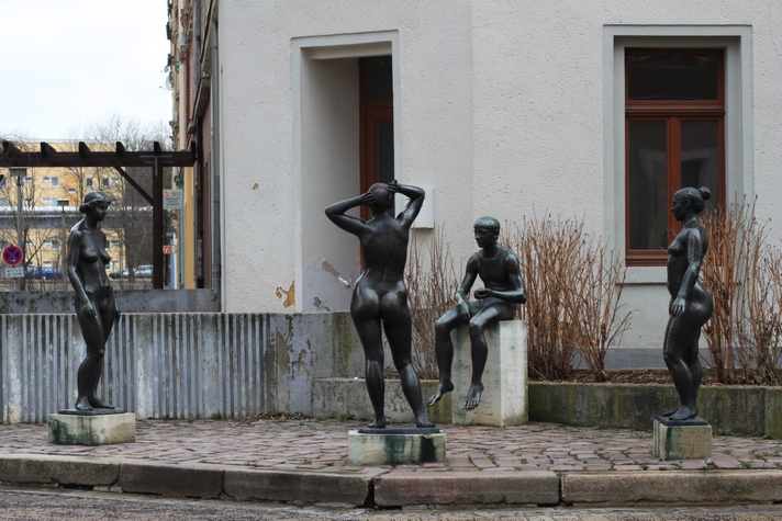 three sculptures of women sit in front of a white building
