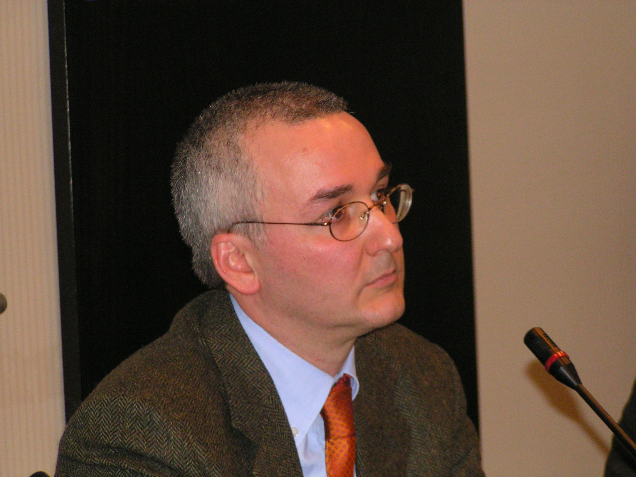 a man wearing glasses and a suit sitting in front of a microphone