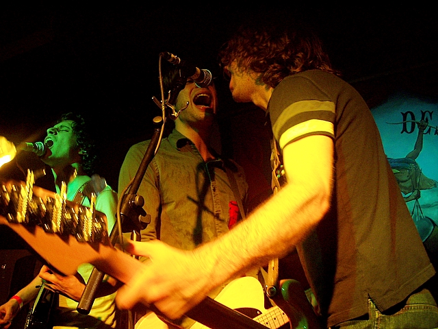 a couple of men singing into microphones near a guitar