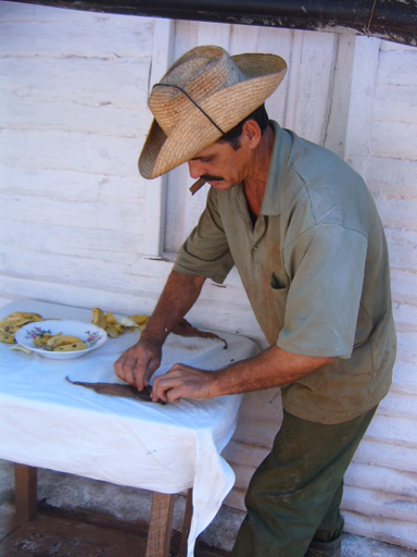 a man wearing a hat cuts a knife with a piece of food on it