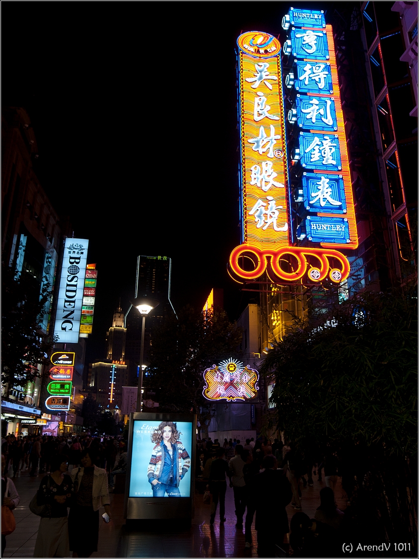 a large neon sign sitting above people on a street