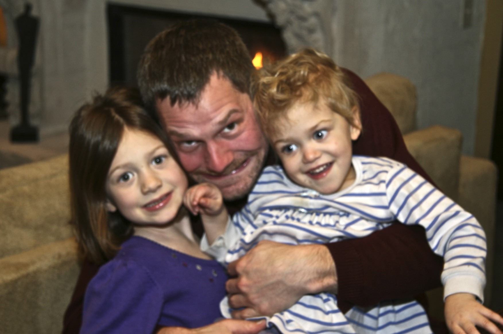a man holds two small children while smiling