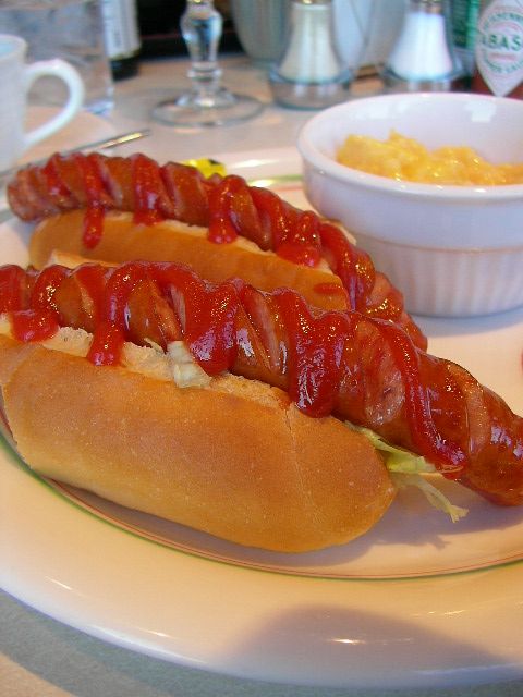 the long  dog is covered in ketchup on the bun