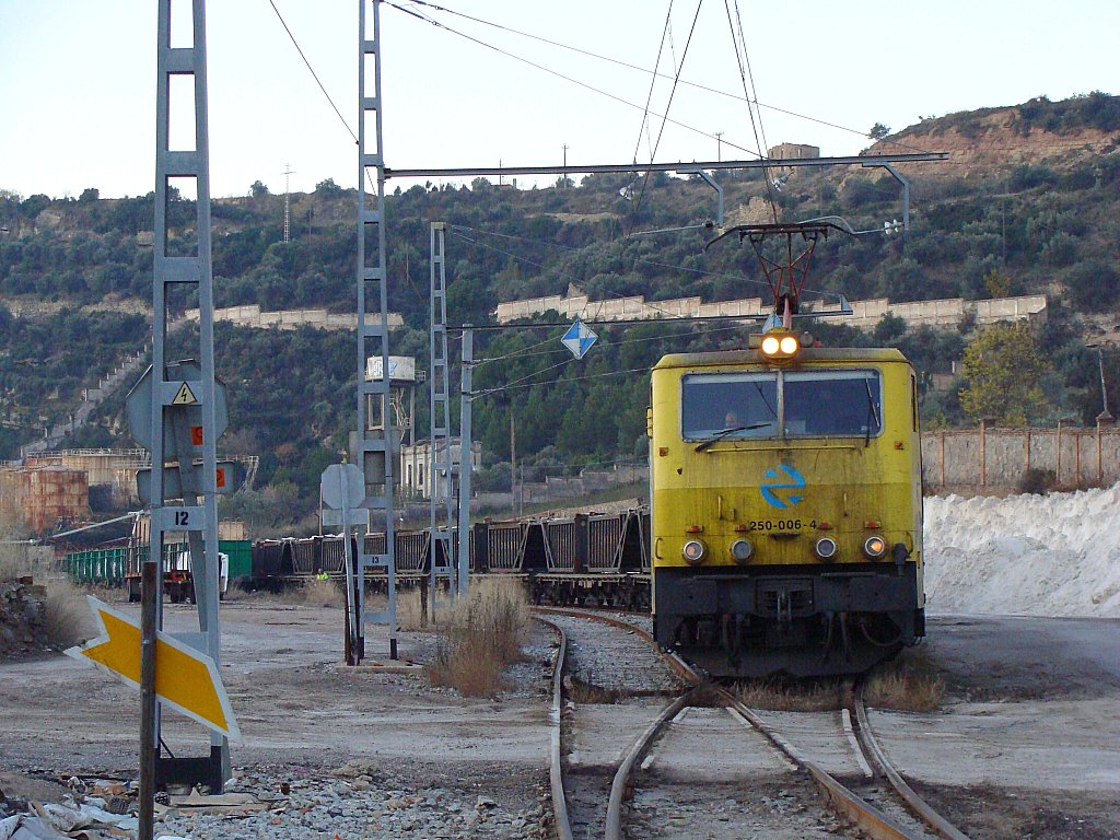 yellow train in rail yard near hill and buildings