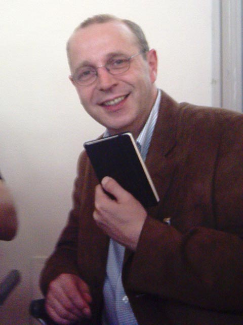a man in a brown jacket and tie holding a black tablet