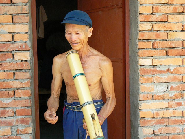 an older man stands with a giant metal tube