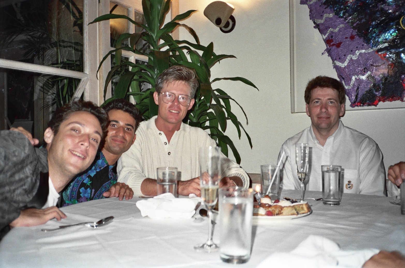 four men sitting around a dinner table in a room with plant