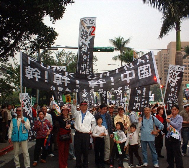 a group of people with asian writing on banners, in the middle of a protest