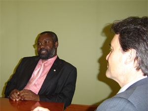 a man wearing a pink shirt sits at a table with another person