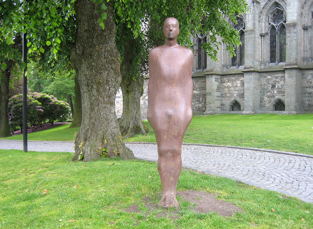 a large standing man statue by the tree in a park