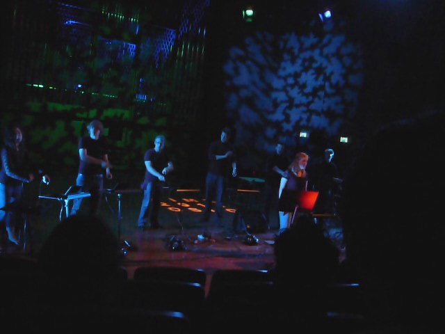people sitting on stage watching performers performing in the dark