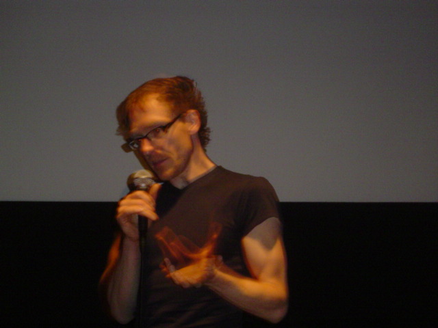 man with dark t - shirt speaking into microphone