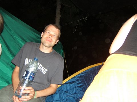 man with a bottle in his hand sitting next to a tent