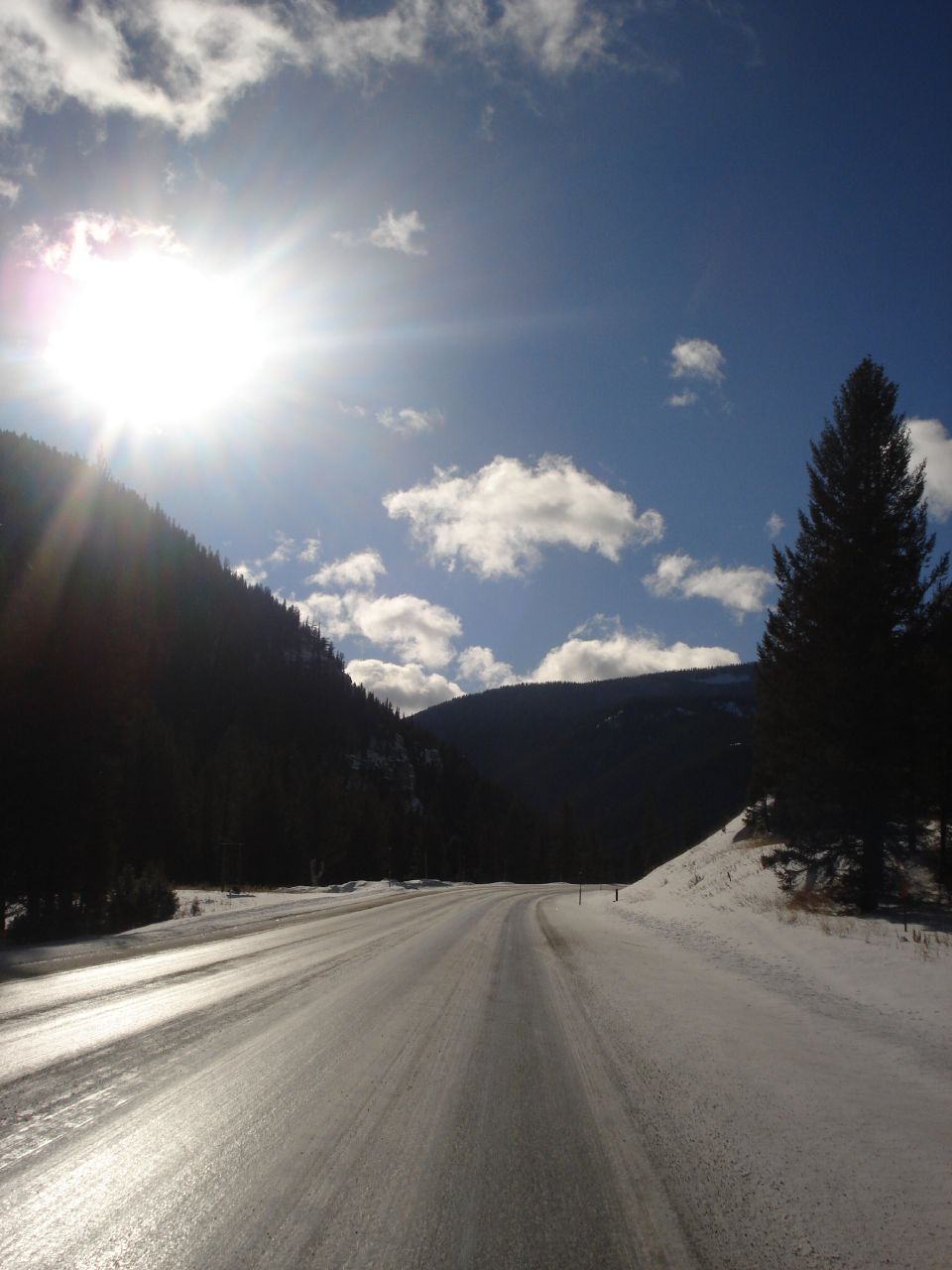 snow - covered road with a bright sun behind it