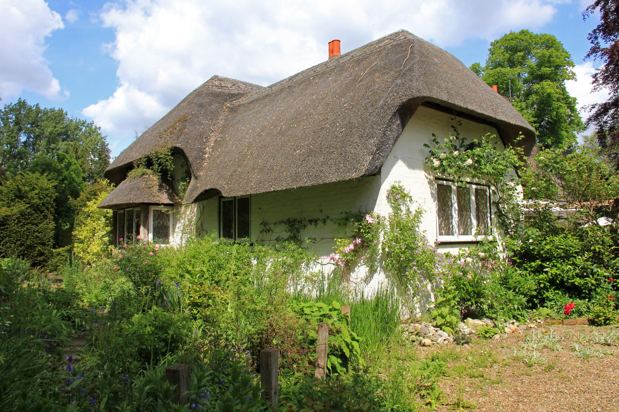 a thatched - roofed white cottage sits in the middle of bushes