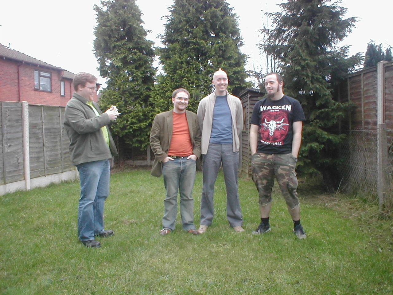 four guys standing in a backyard outside taking a picture with their cell phone