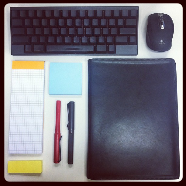 black computer keyboard, mouse, notepad, binder, and pen on a white desk