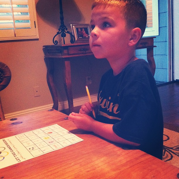 a little boy writing on a table with a scrabble game in front of him