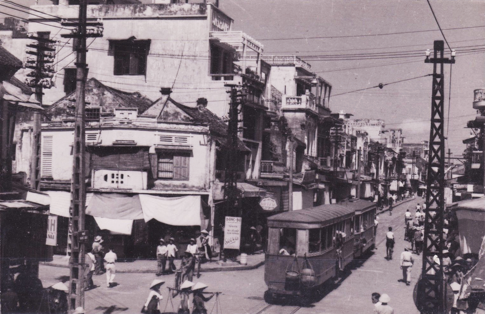 an old street scene shows people, buildings and trams