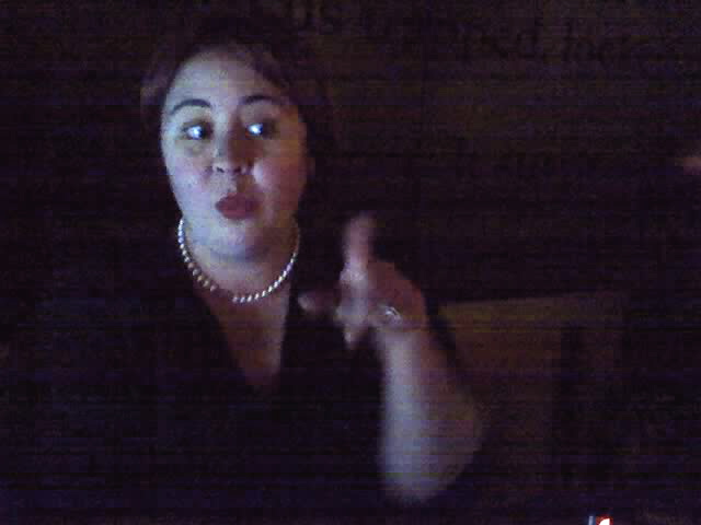 a lady with a pearl necklace gesturing at the camera