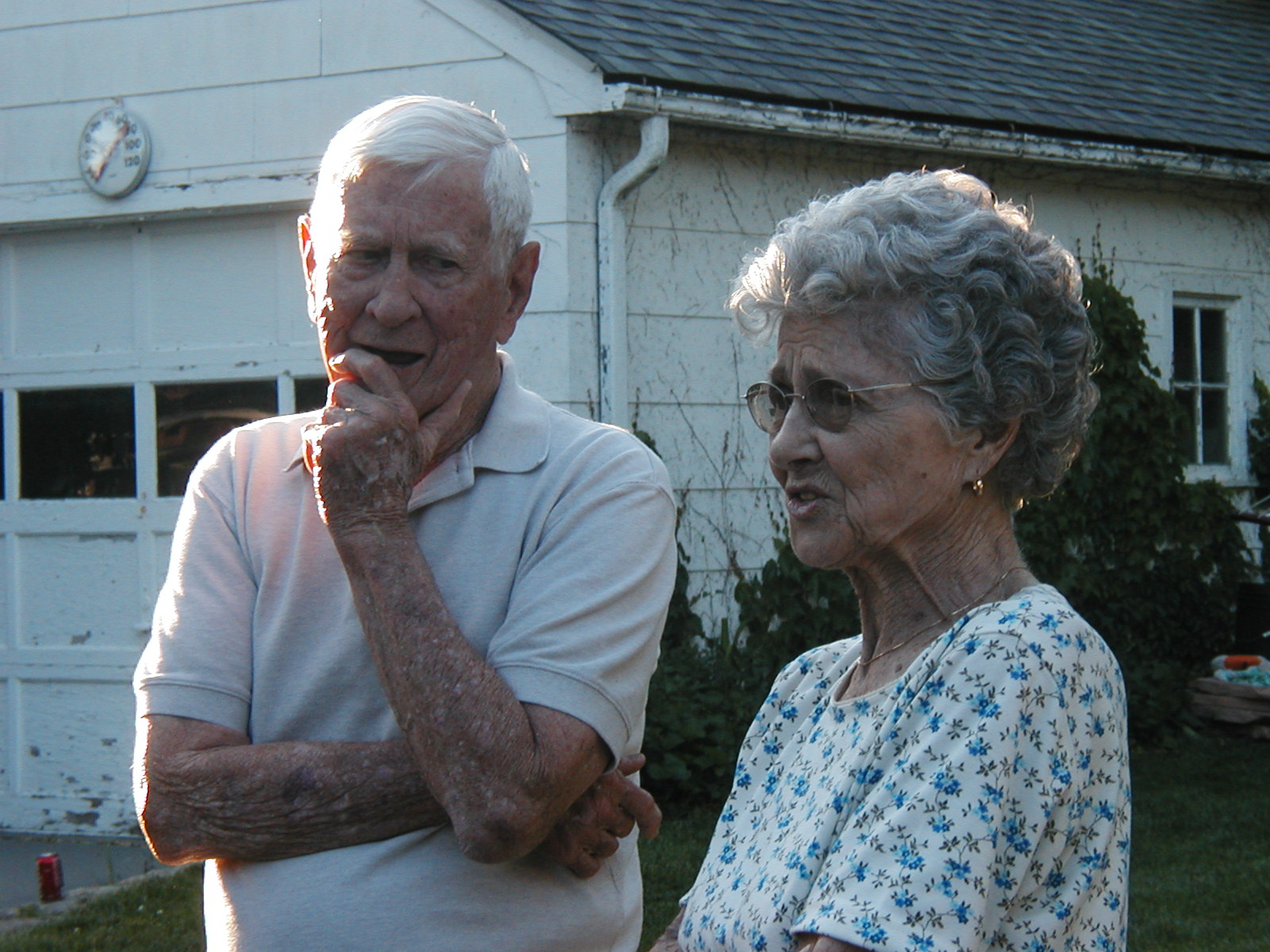 two elderly people are standing in front of a house