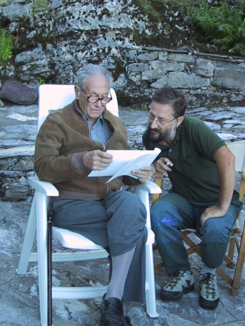 two men sit in white chairs outside on the rocks