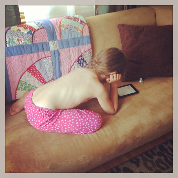 a child is sitting on a couch looking at a tablet