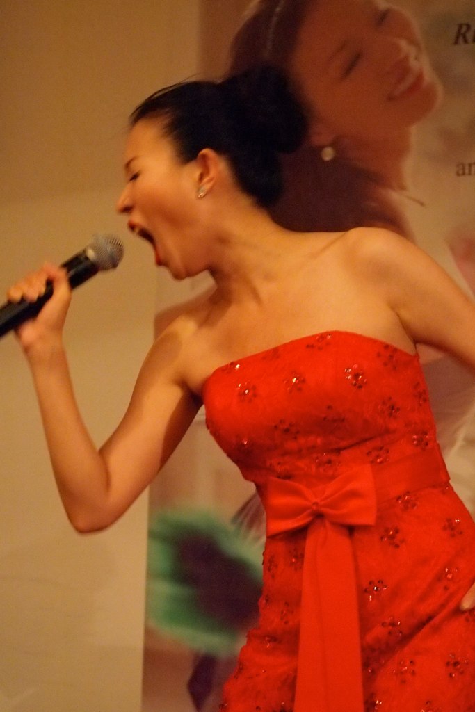 woman wearing red singing into a microphone while holding her arm over her chest