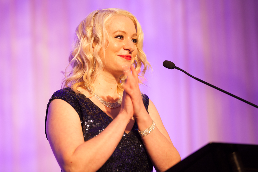 a woman stands at a podium and looks upward while making a gesture