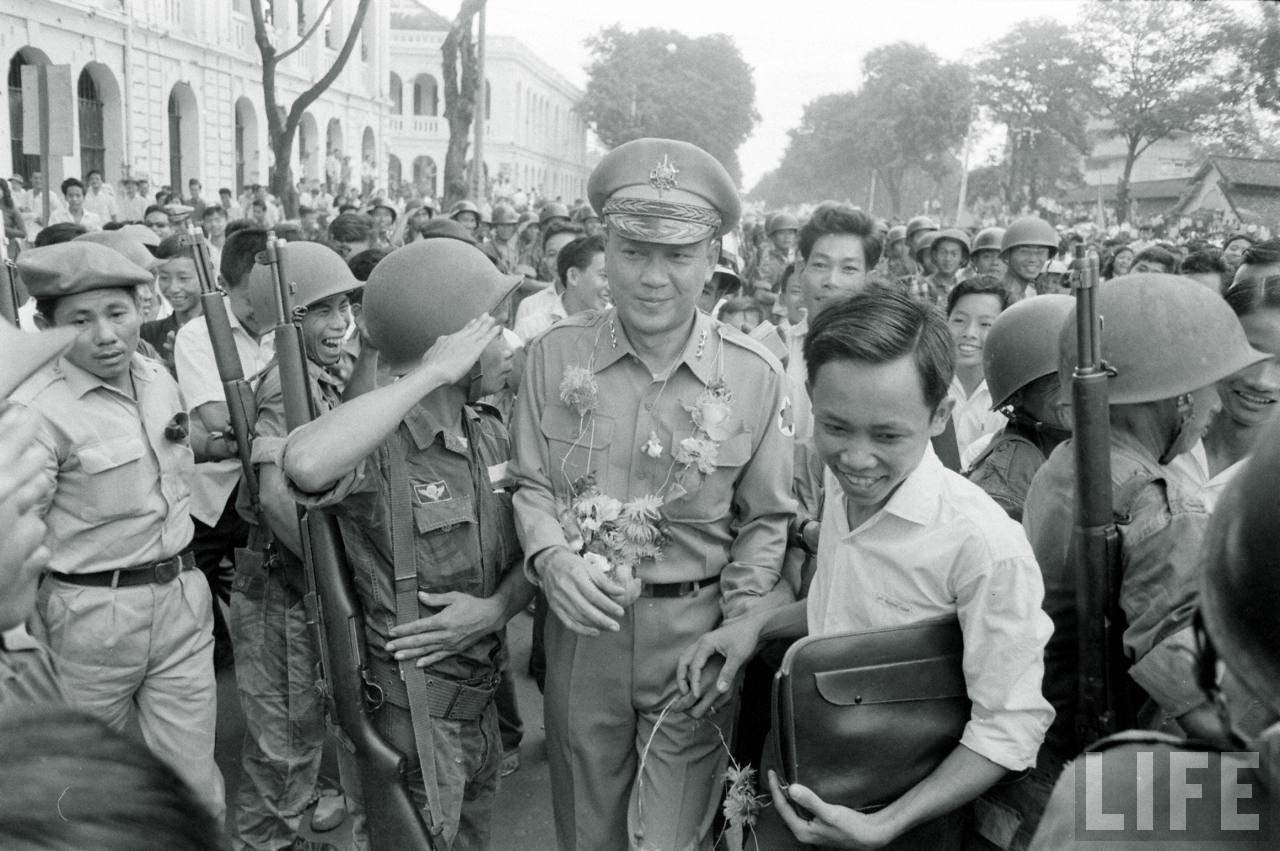 an army officer walking behind several men with guns