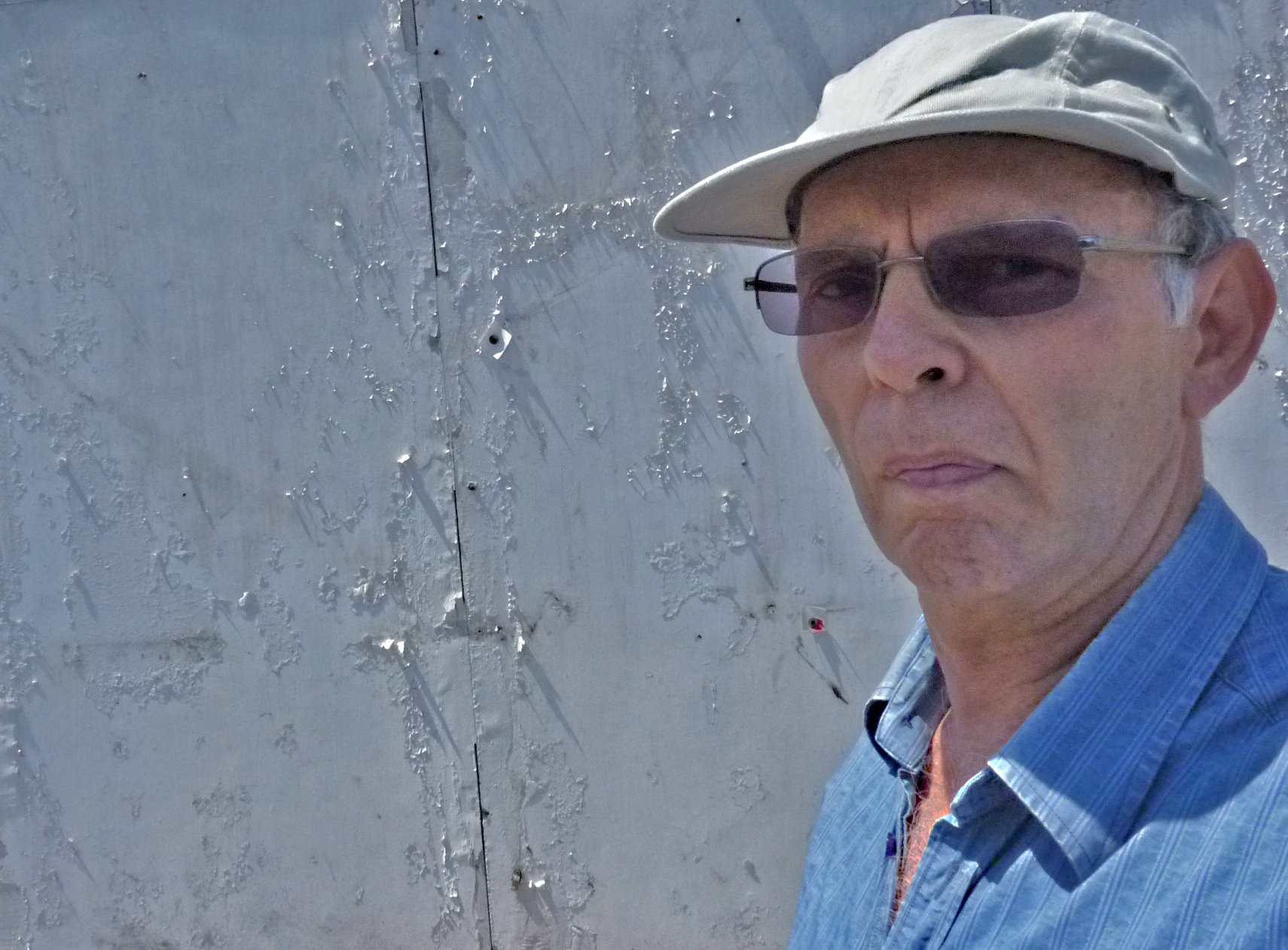 an elderly man wearing a hat and glasses standing in front of water fountain