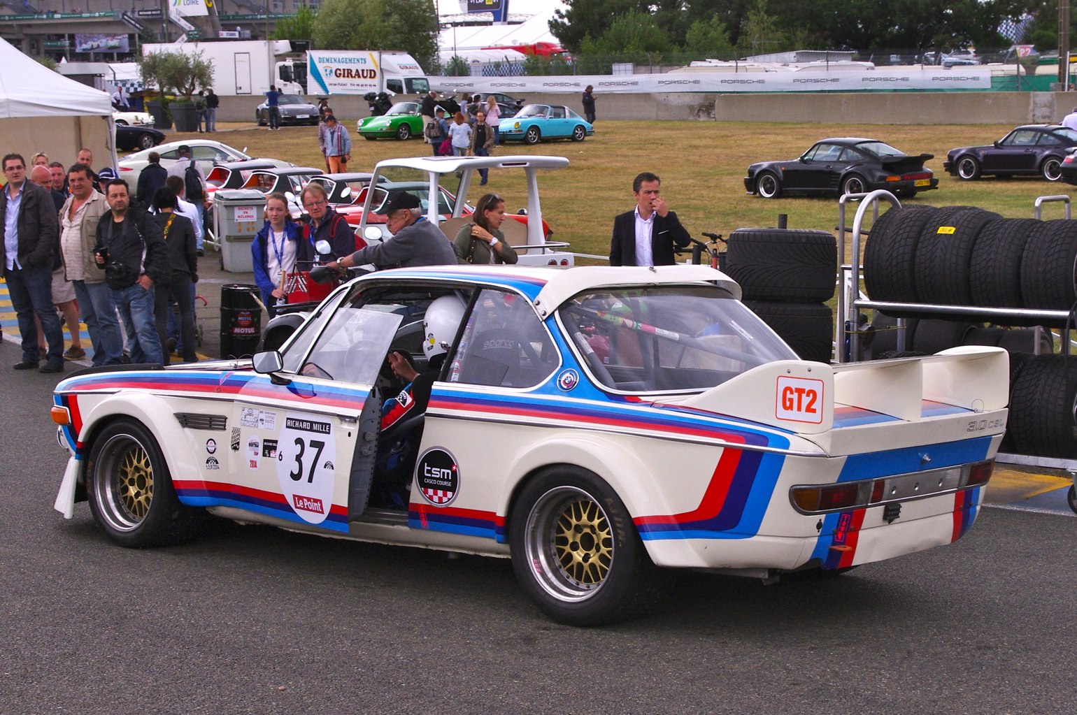 a white, blue and red race car driving past some people