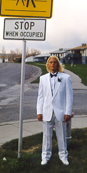 man dressed up in tuxedo with white bow tie next to street sign
