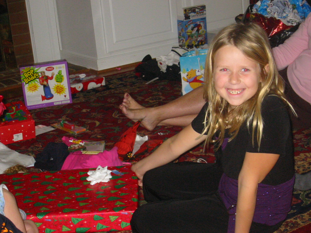 a smiling  in black shirt sitting on the floor with presents