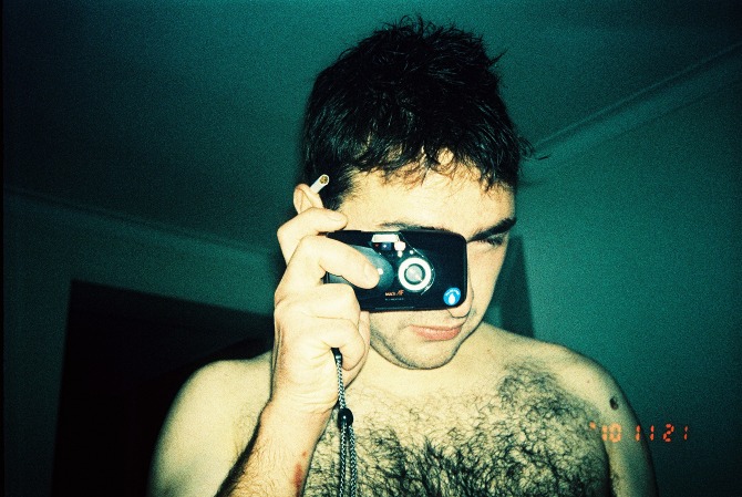 man with hairy chest holding camera while talking on cell phone