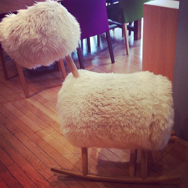 a sheepskin chair with two round stools, sitting on a wooden floor
